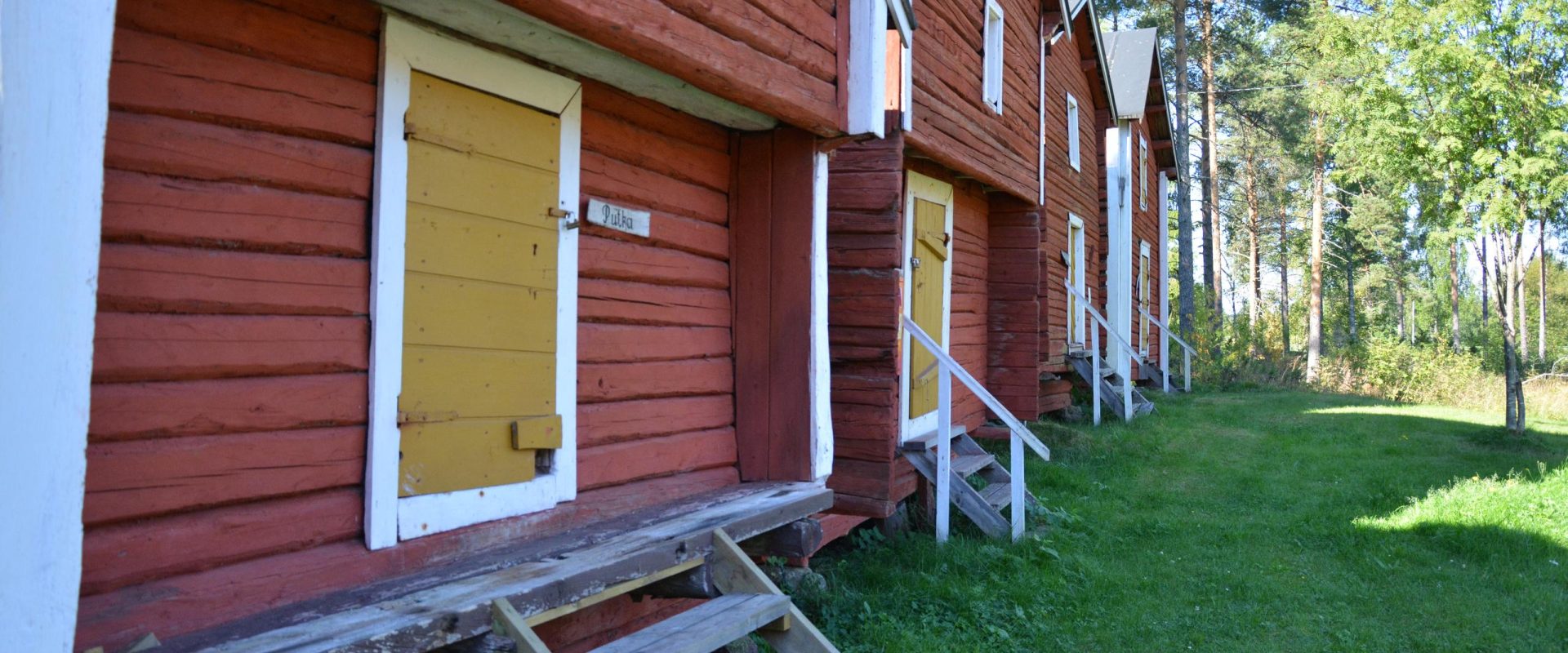 Punainen hirsirakennus, jonka ikkunaluukut ovat keltaiset