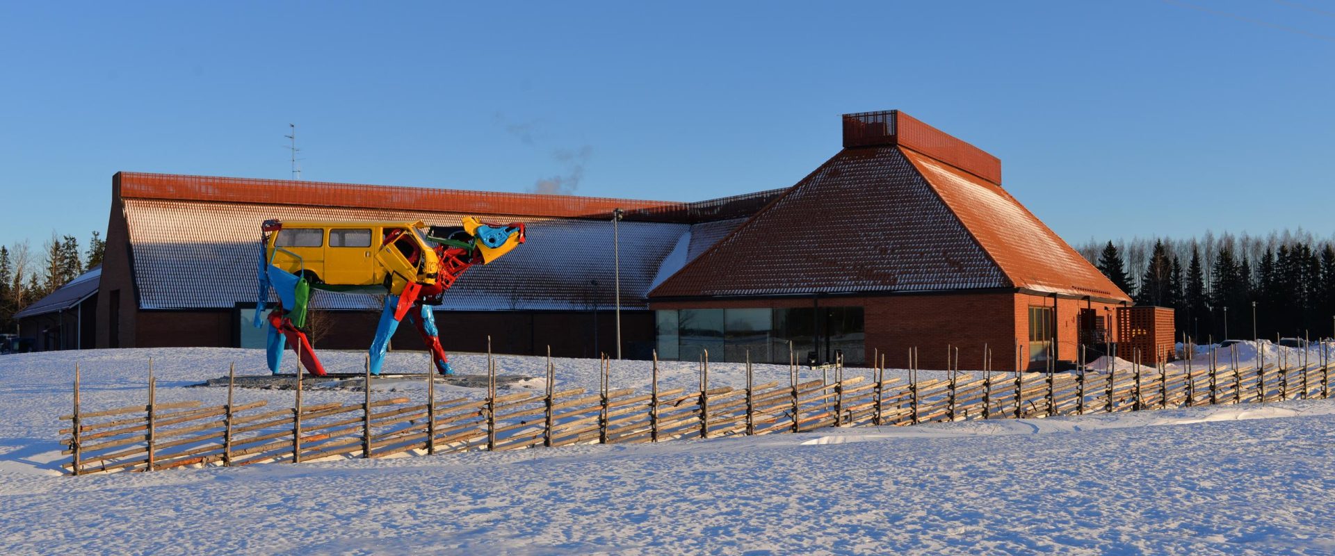 Museorakennus ja värikäs lehmäveistos lumisessa maisemassa
