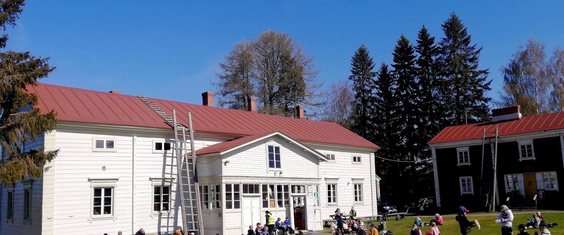 Rovaniemen kotiseutumuseon valkoinen päärakennus ja nurmikolla istuvia ihmisiä